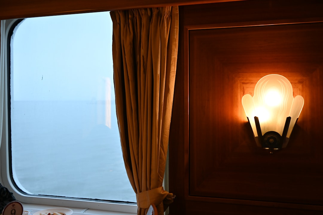 luxury train journeys redefine — a private wood-paneled sleeping suite with golden lamp light and landscape passing outside the window at dusk