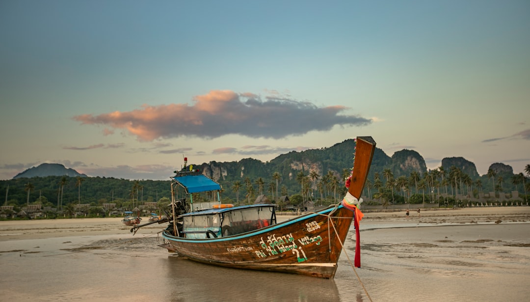 hidden coastal destinations asia — wooden longtail boat moored near a limestone karst island at golden hour