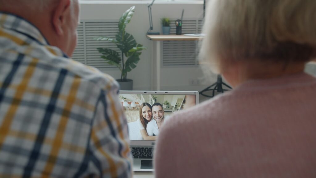 Happy senior parents are talking to young couple using laptop making video call showing thumbs-up at home. communication and technology concept.