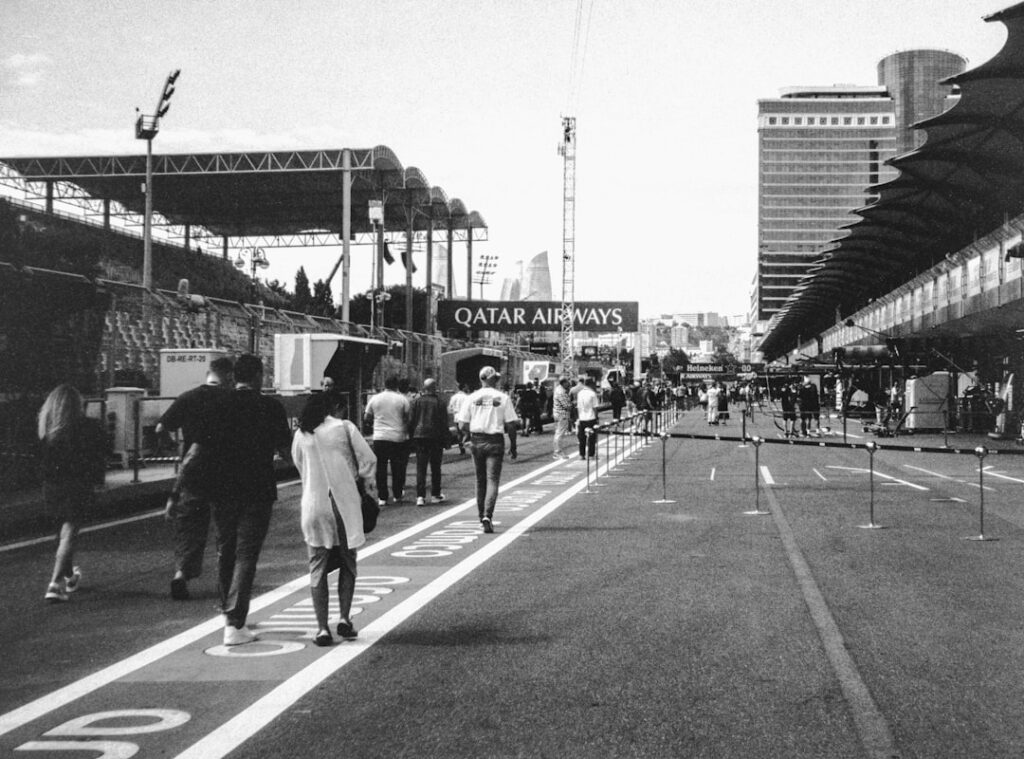 People walking on a race track with grandstands and buildings.