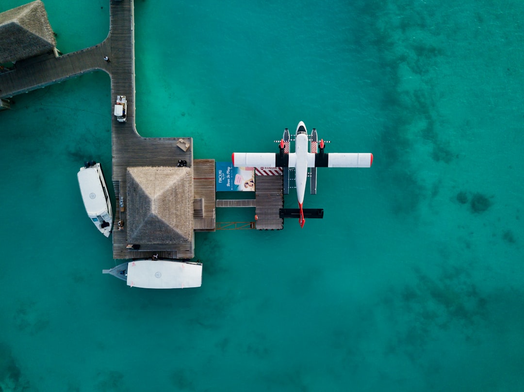 rise remote island tourism — aerial view of seaplane landing near overwater resort bungalows